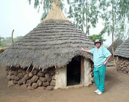 Dr. Doshier standing next to rural Senegal thatch hut